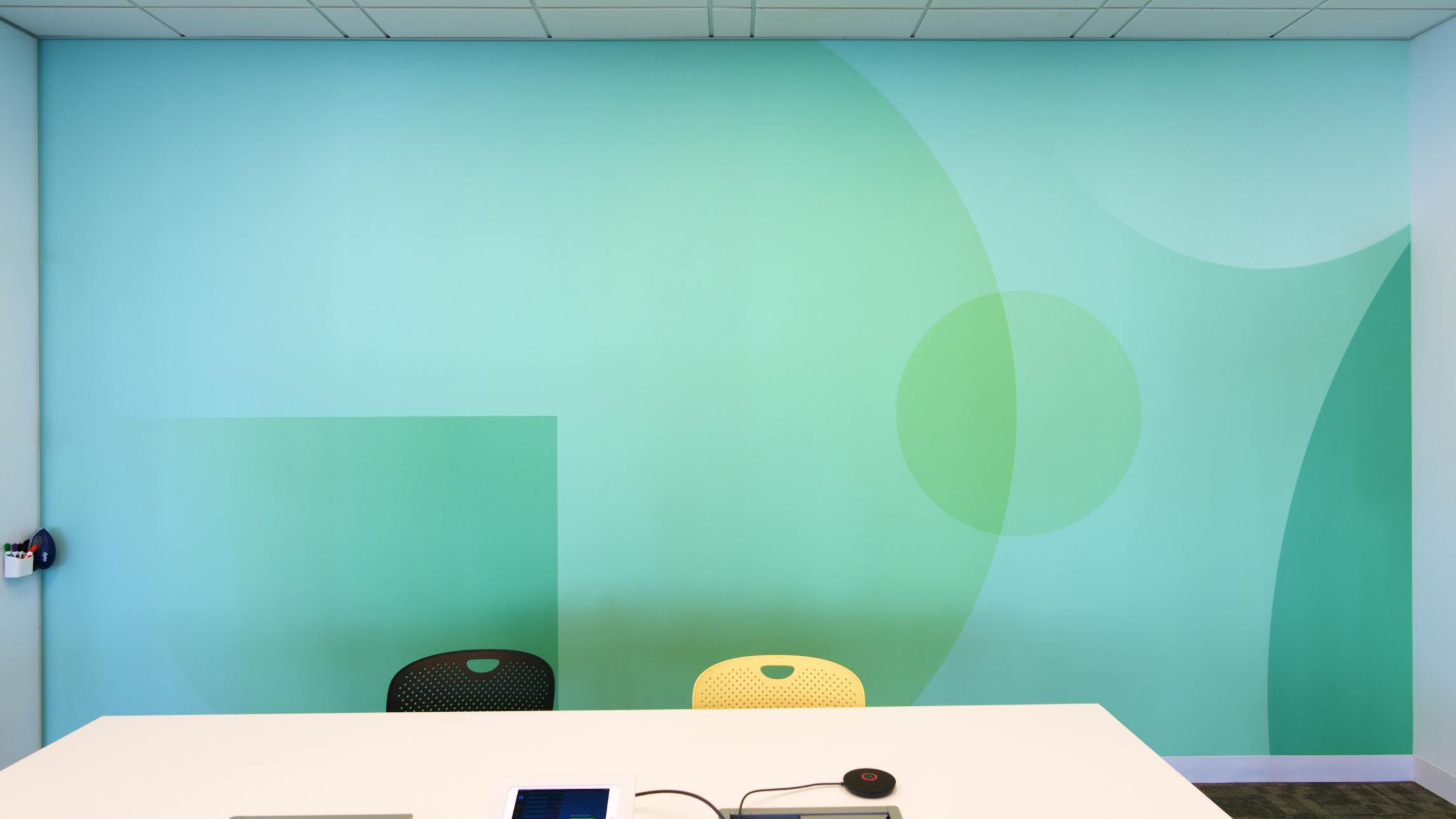 A photograph of the inside of a Datadog conference room- the focal point being a wall with custom wallpaper. The wallpaper is monochramatic and cyan and comprised of layered circles and sqaures of varying sizes and opacities.