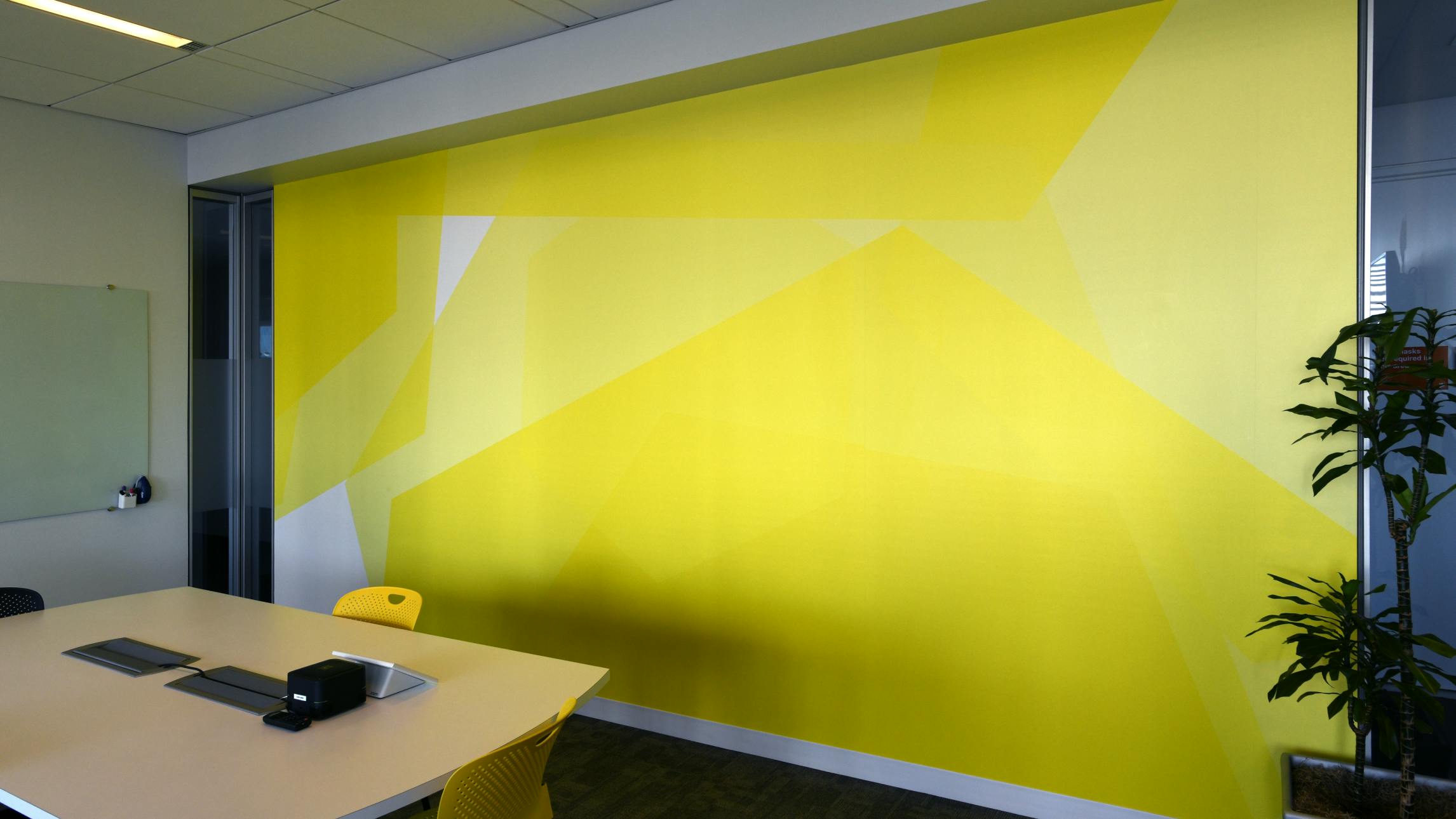 A photograph of the inside of a Datadog conference room- the focal point being a wall with custom wallpaper. The wallpaper is monochramatic and yellow and comprised of oversized hexagons layered at varying angles.