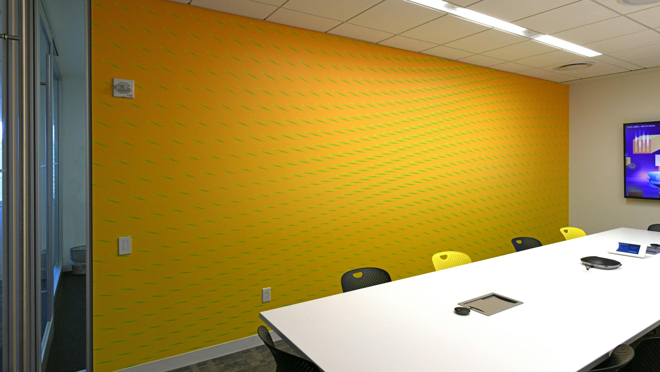 A Datadog conferene room with a custom wallpaper. Th wallpaper is yellow and has many green dashes arranged at varying angles, similar to the digital rendering above.